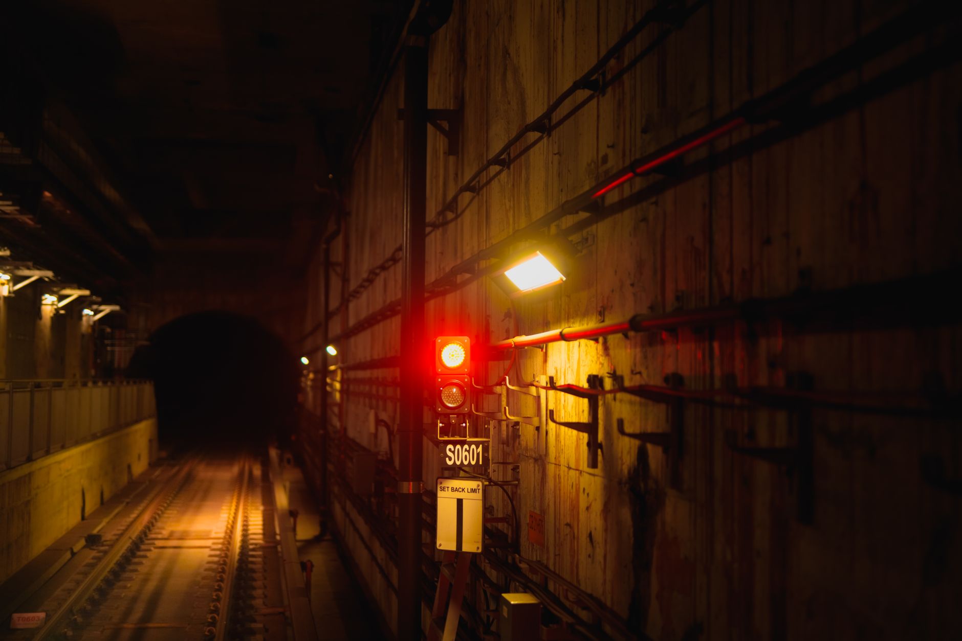 A dimly lit subway tunnel featuring a bold red signal light casting shadows on the gritty walls.