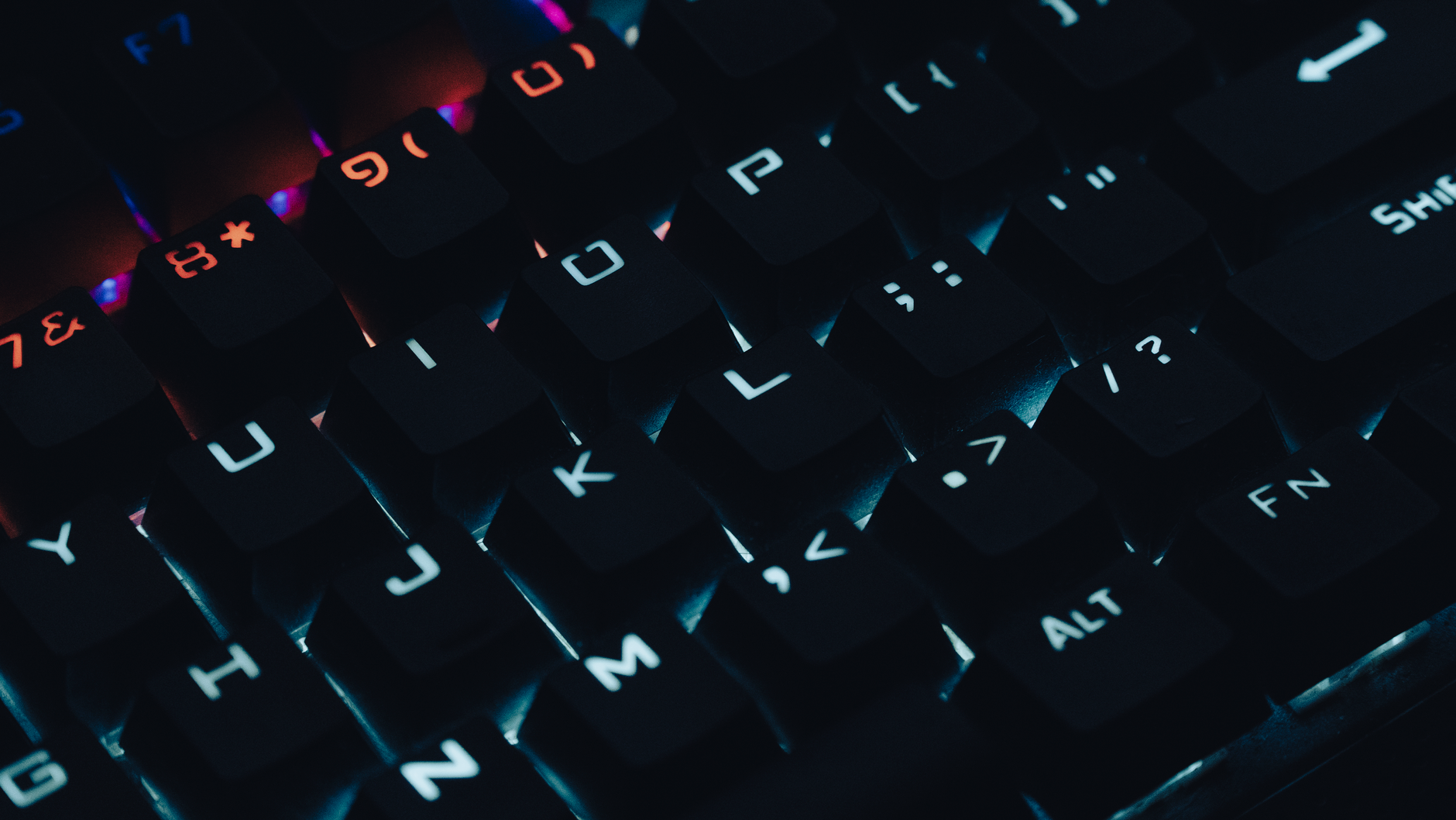 Dark, close-up image of a backlit mechanical keyboard with glowing keys.