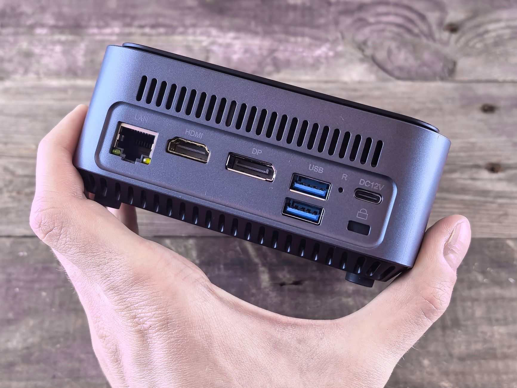 A compact desktop computer held in a hand, showing its ports.
